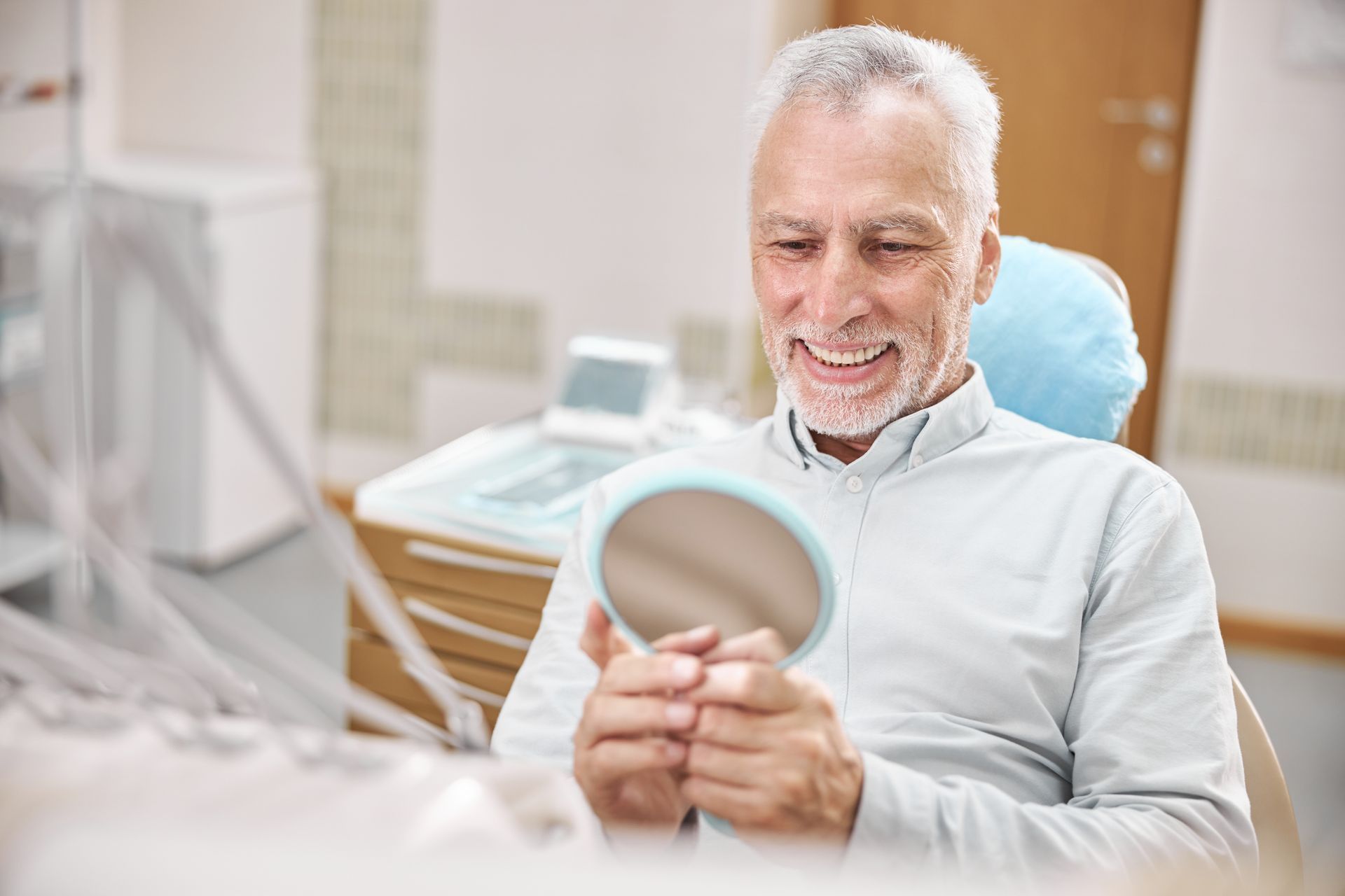 Smiling man in a dental chair holding a dental mirror in a bright clinic Smiling man in a dental chair holding a dental mirror in a bright clinic