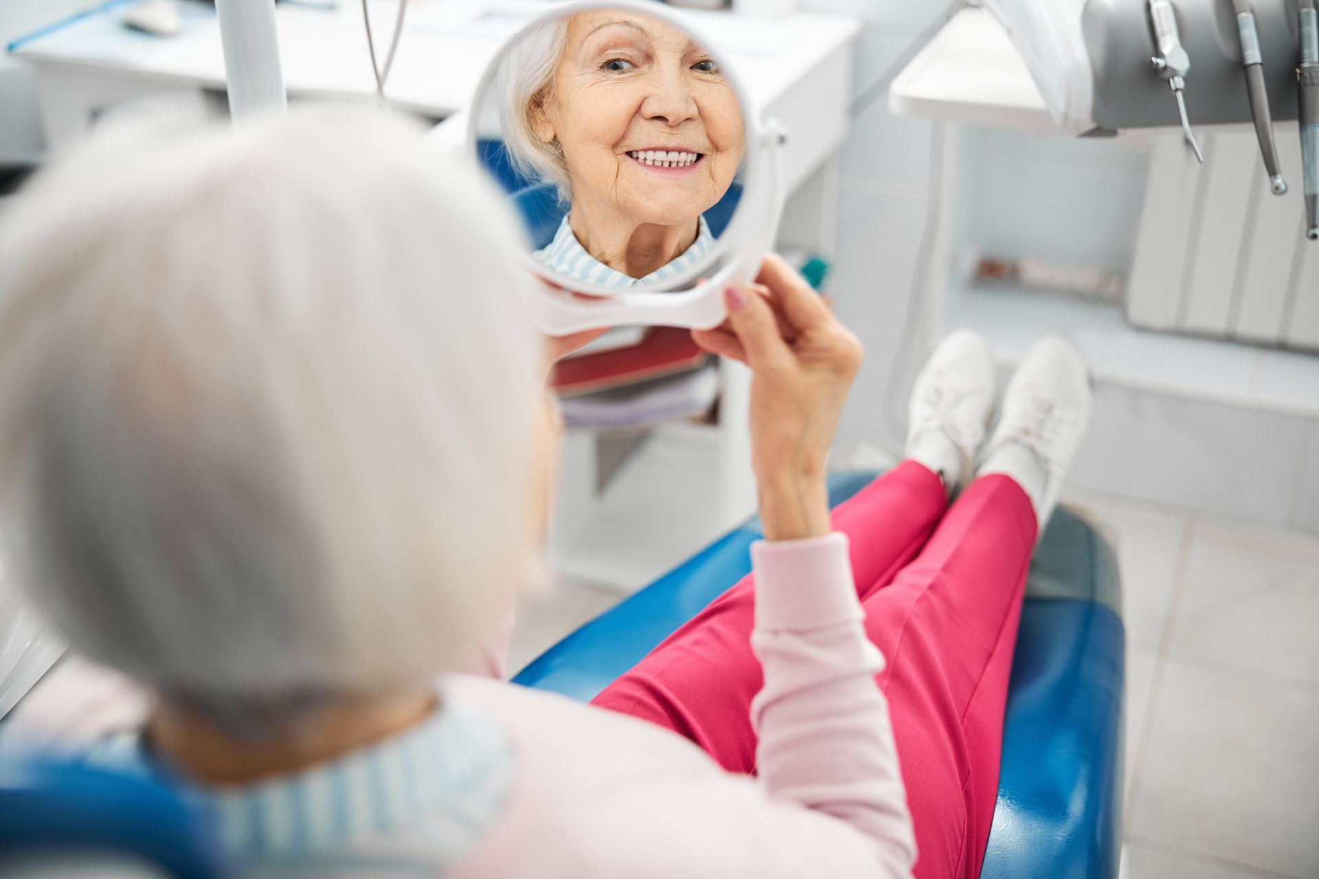 Dental patient looking in a mirror while reclining in a dentist chair, smiling in a bright clinic. Dental patient looking in a mirror while reclining in a dentist chair, smiling in a bright clinic.