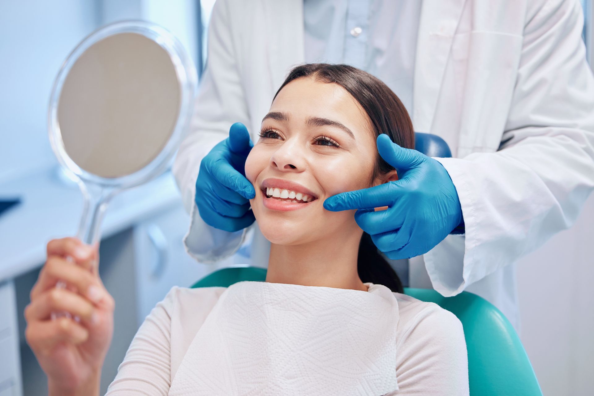 Patient smiling during a dental exam while a dentist in blue gloves checks her teeth with a mirror. Patient smiling during a dental exam while a dentist in blue gloves checks her teeth with a mirror.