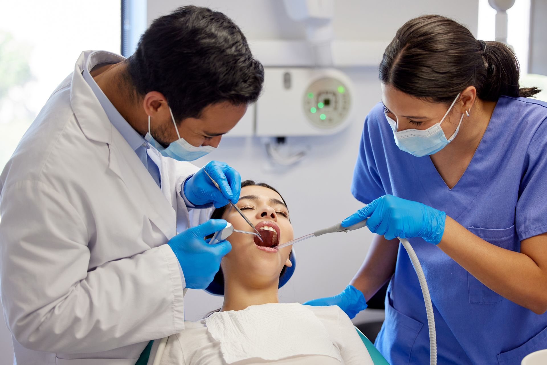 Dentist and assistant treating a patient in a dental clinic, using tools while the patient lies back in a chair.