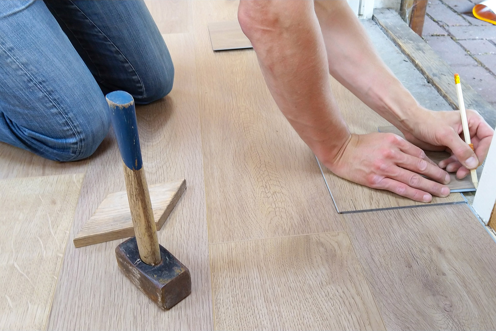 A person is measuring a piece of wood next to a hammer and pencil.