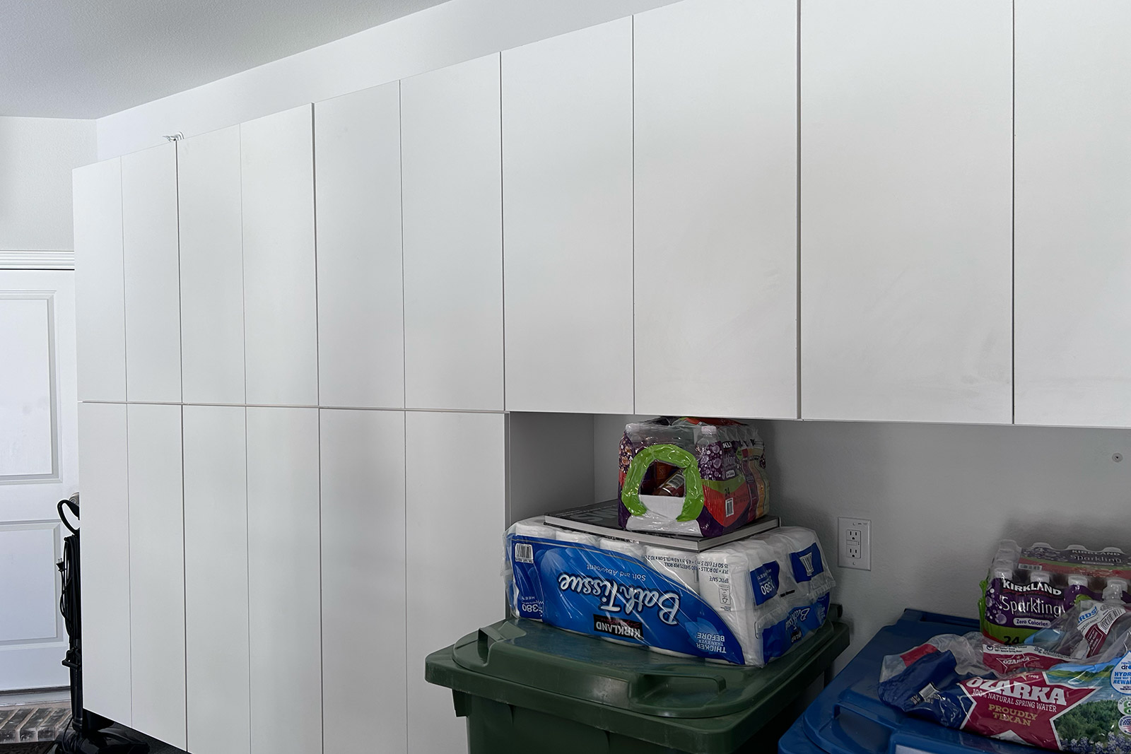 A room with a lot of white cabinets and trash cans.