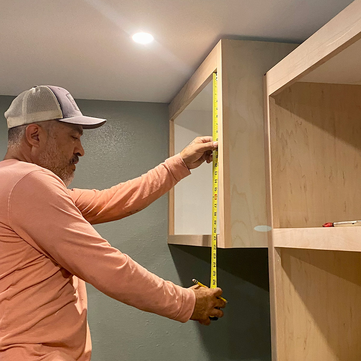 A man is measuring a cabinet with a tape measure