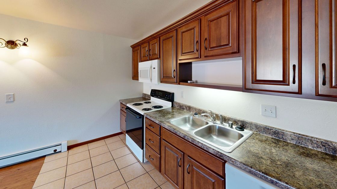 Empty kitchen with wooden cabinets, granite counters, white stove, double sink, and tiled floor