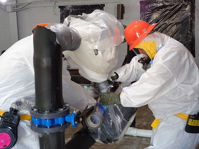 Workers in protective suits repairing pipes in an industrial setting