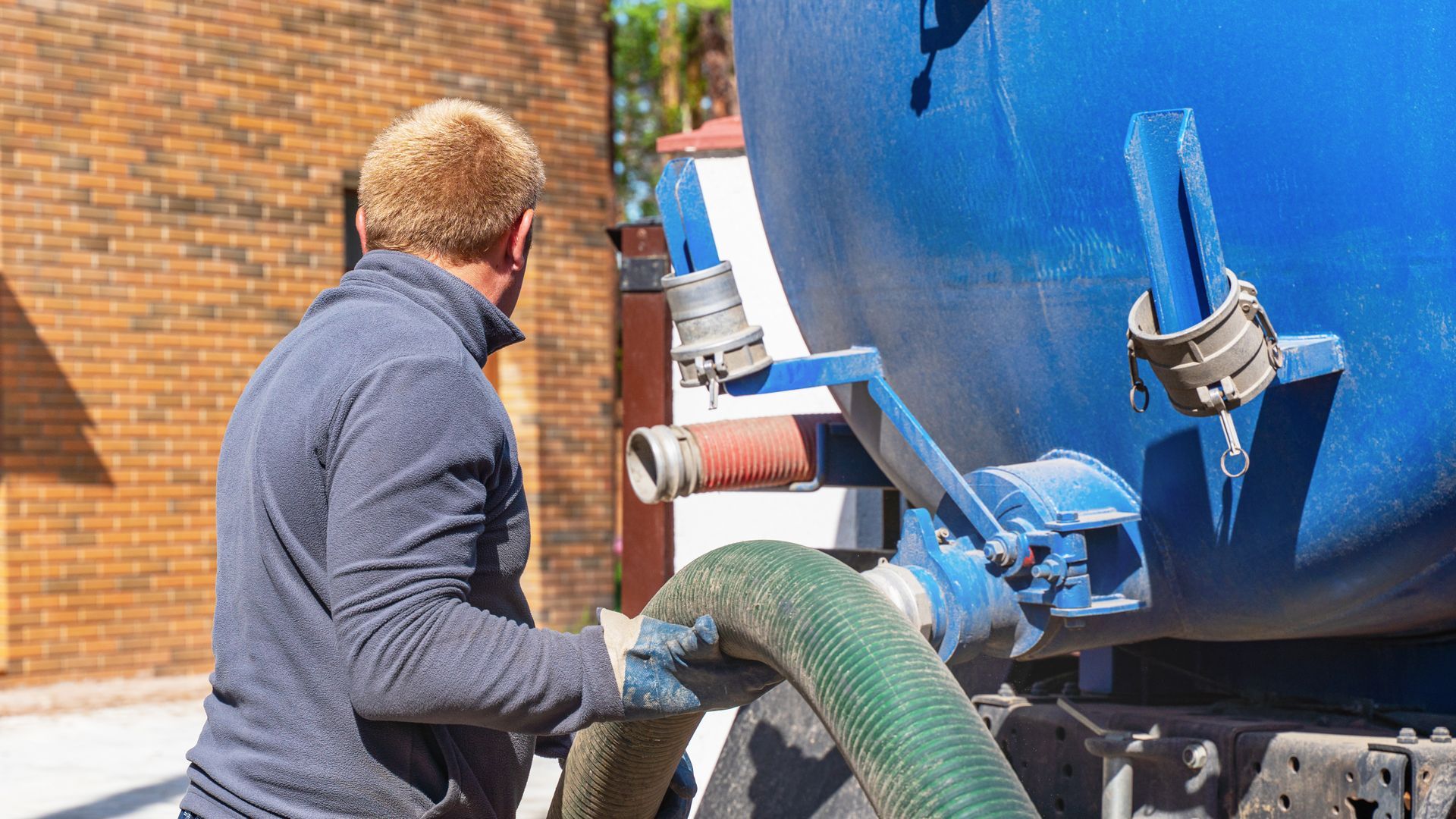 Worker emptying septic tank with a vacuum pipe Septic tank service worker operating sewage tank truck.