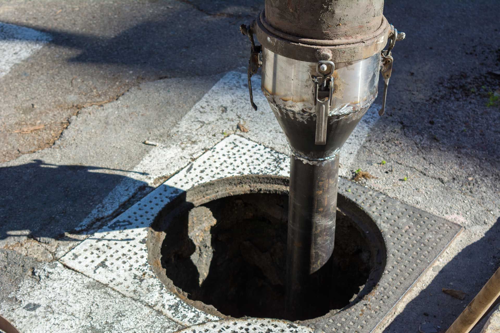 A vacuum hose deposits contents into an open manhole on a city street.