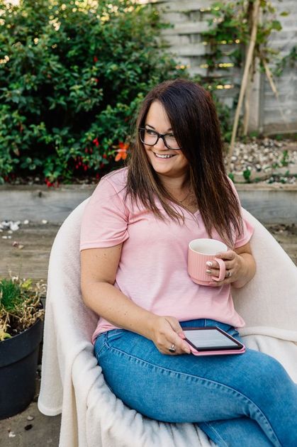 A woman is sitting in a chair holding a cup of coffee and a tablet.