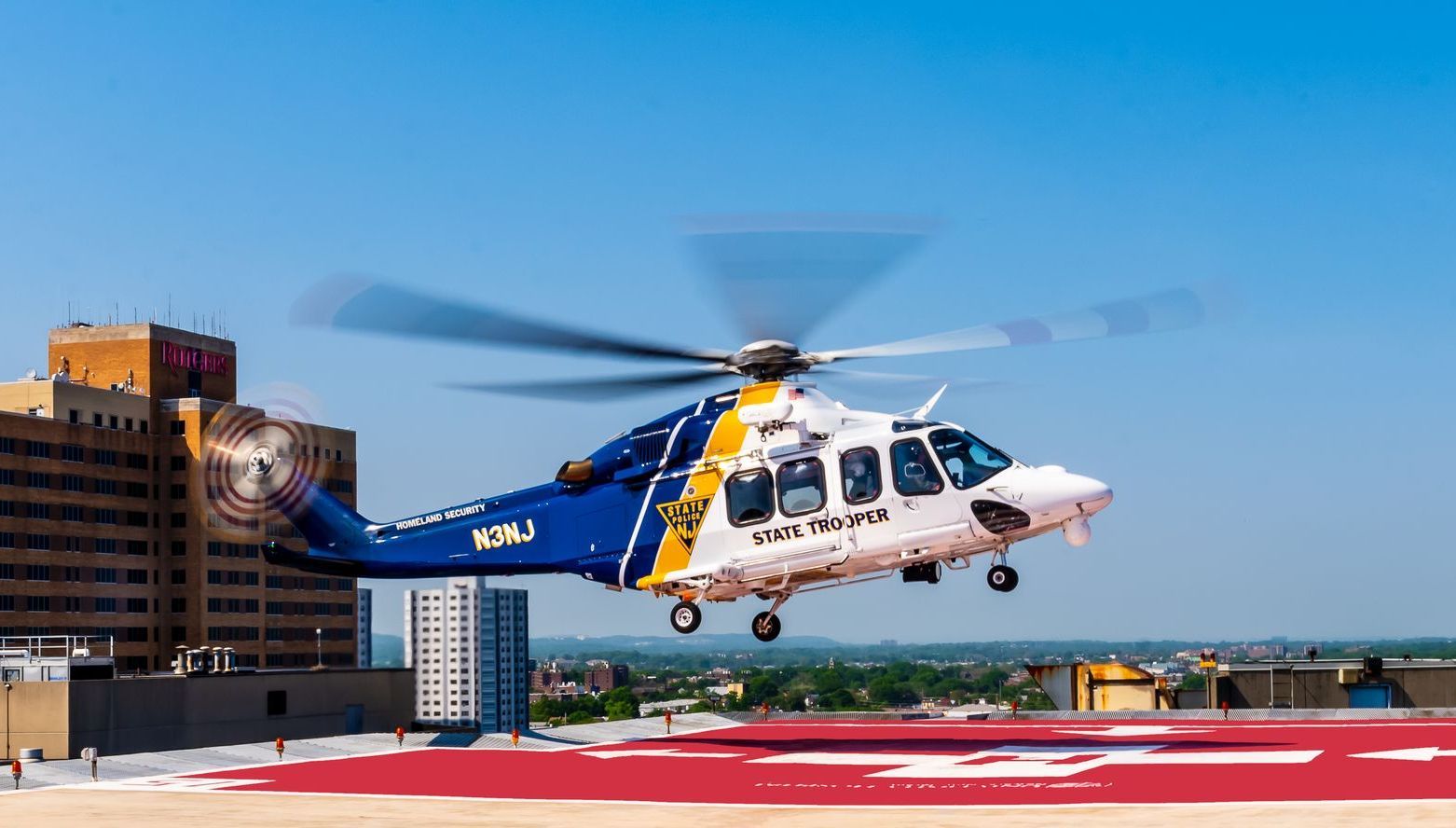 A blue and white helicopter is taking off from a helipad.