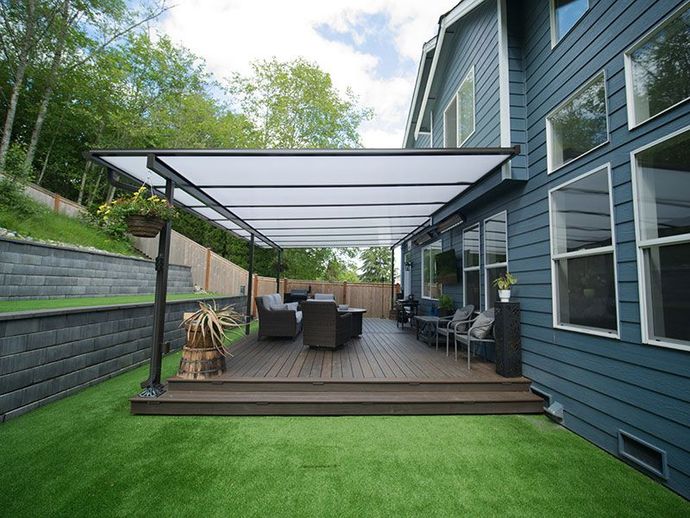 Modern backyard deck with pergola, outdoor seating, and green lawn beside a blue house