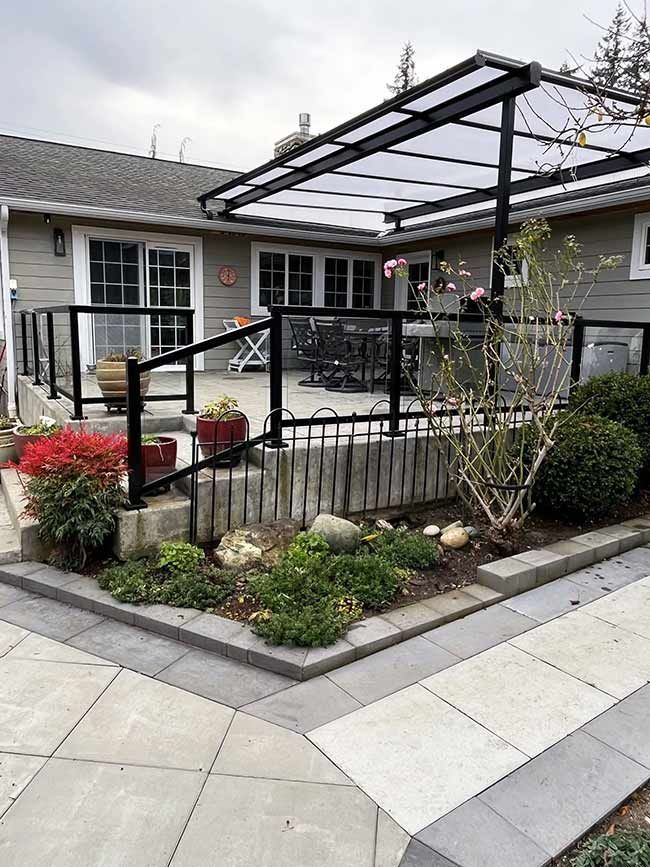 Backyard patio with a black railing, clear roofing, and landscaping.