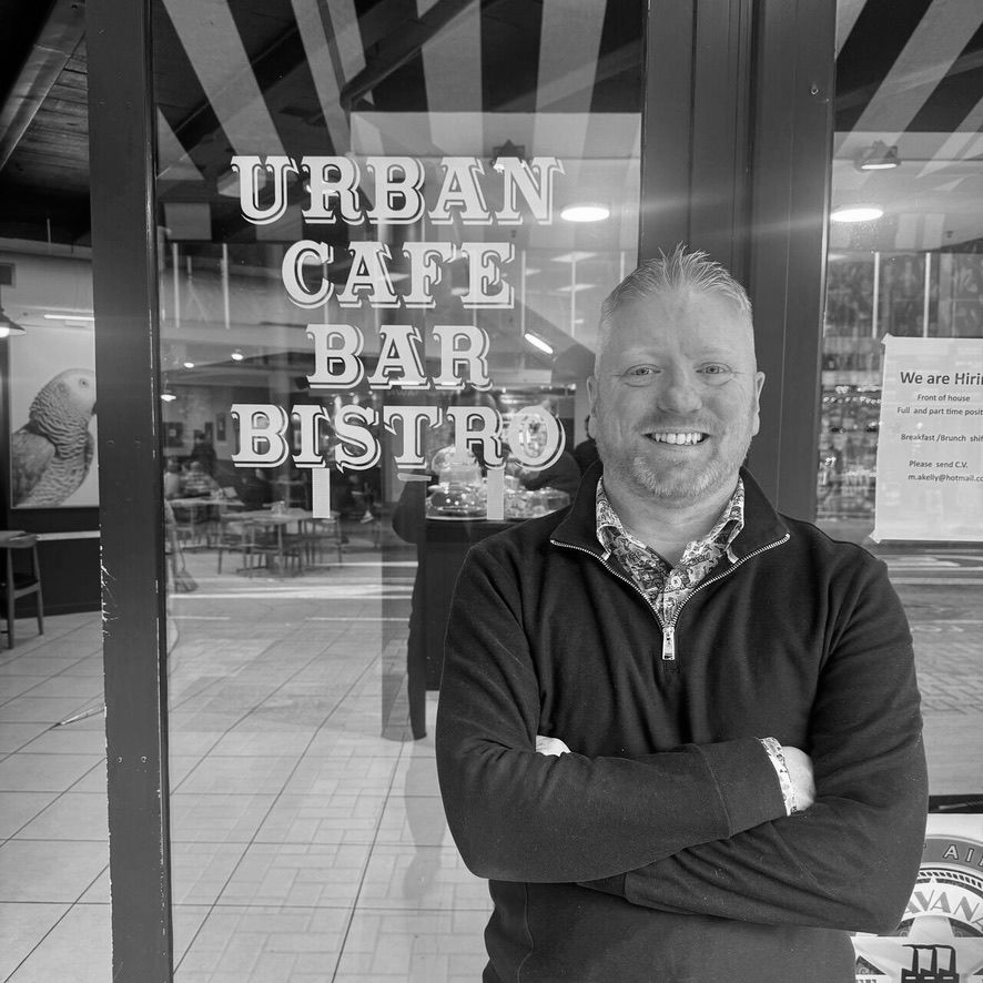 Smiling man with arms crossed standing outside Urban Cafe Bar Bistro sign