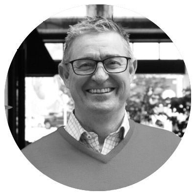 Black-and-white portrait of a smiling bald man in glasses wearing a plaid blazer.
