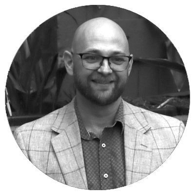 Black-and-white portrait of a smiling bald man in glasses wearing a plaid blazer.