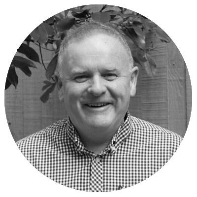 Black-and-white portrait of a smiling bald man in glasses wearing a plaid blazer.
