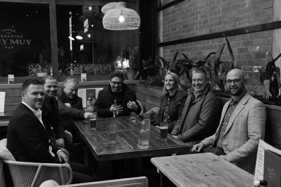 Five people seated around a table in a cozy indoor restaurant or café, smiling at the camera.