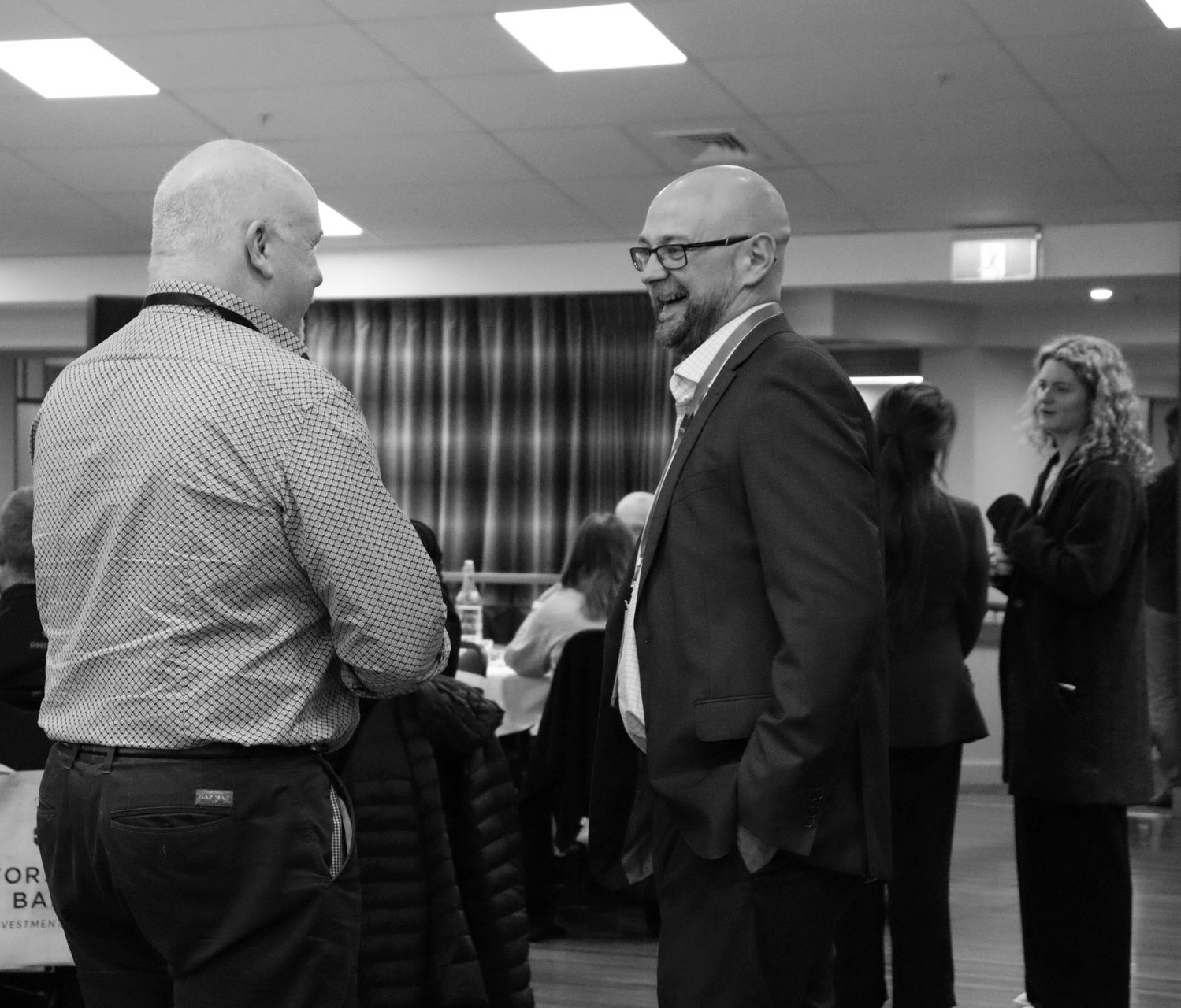 Two men in business attire chat at a networking event in a bright conference room.