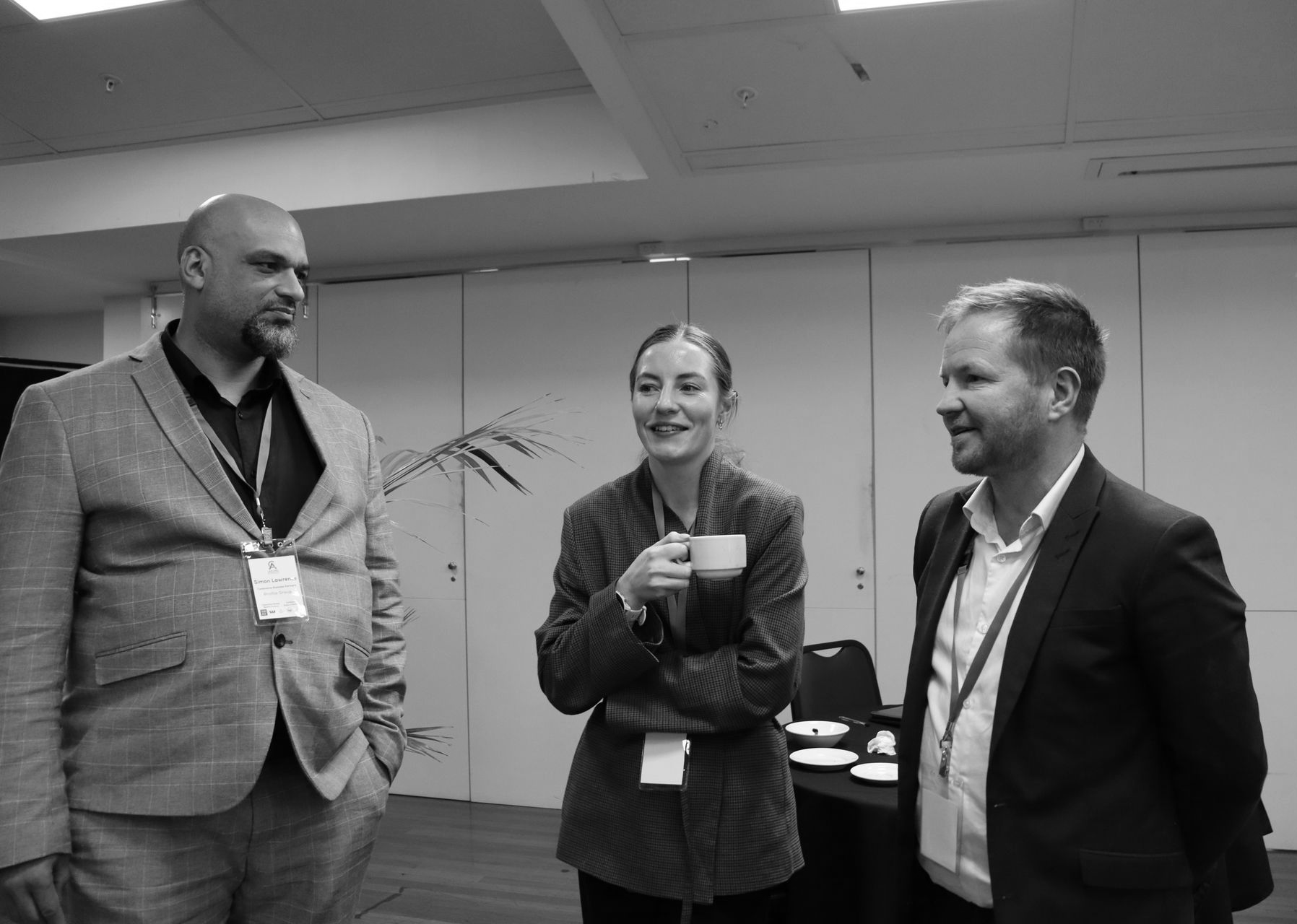 Three people in a meeting room discussing a tablet across a conference table.