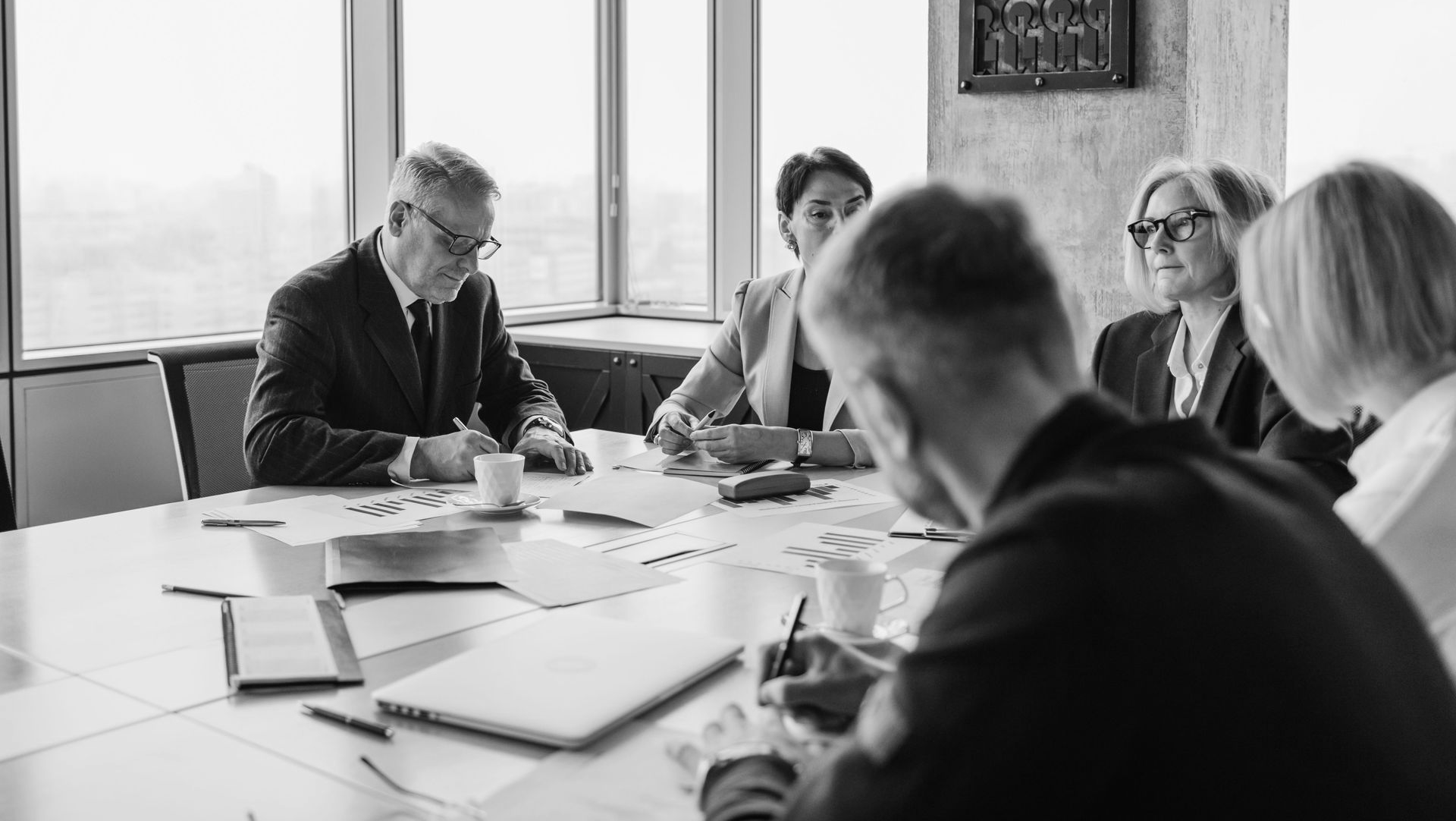 People in a meeting around a conference table, discussing papers in a bright office.