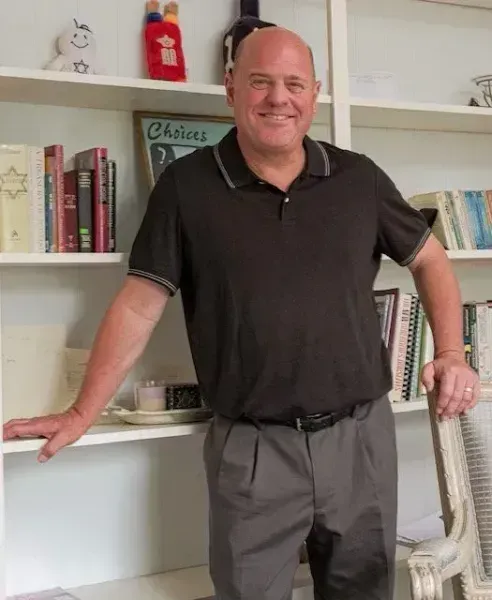 A man in a black shirt is standing in front of a bookshelf