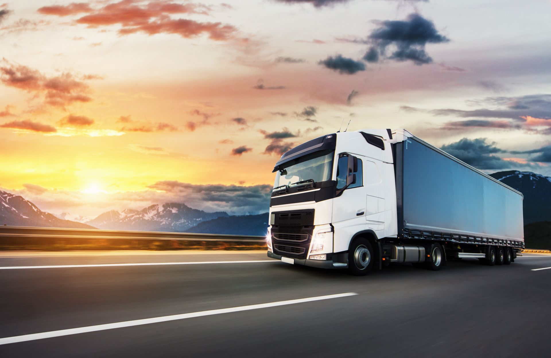White semi-truck driving on a highway at sunset.
