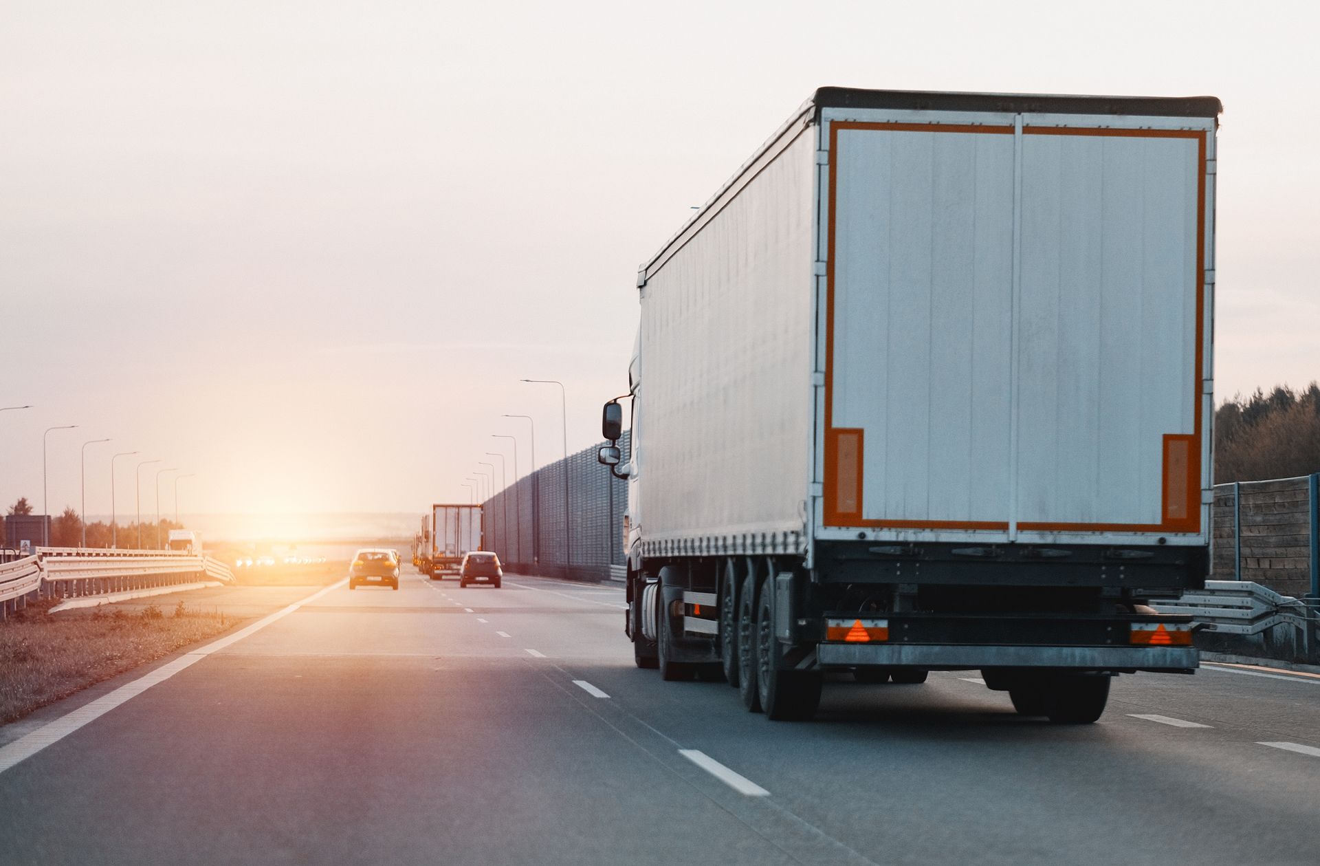 A semi-truck drives on a highway towards the setting sun.