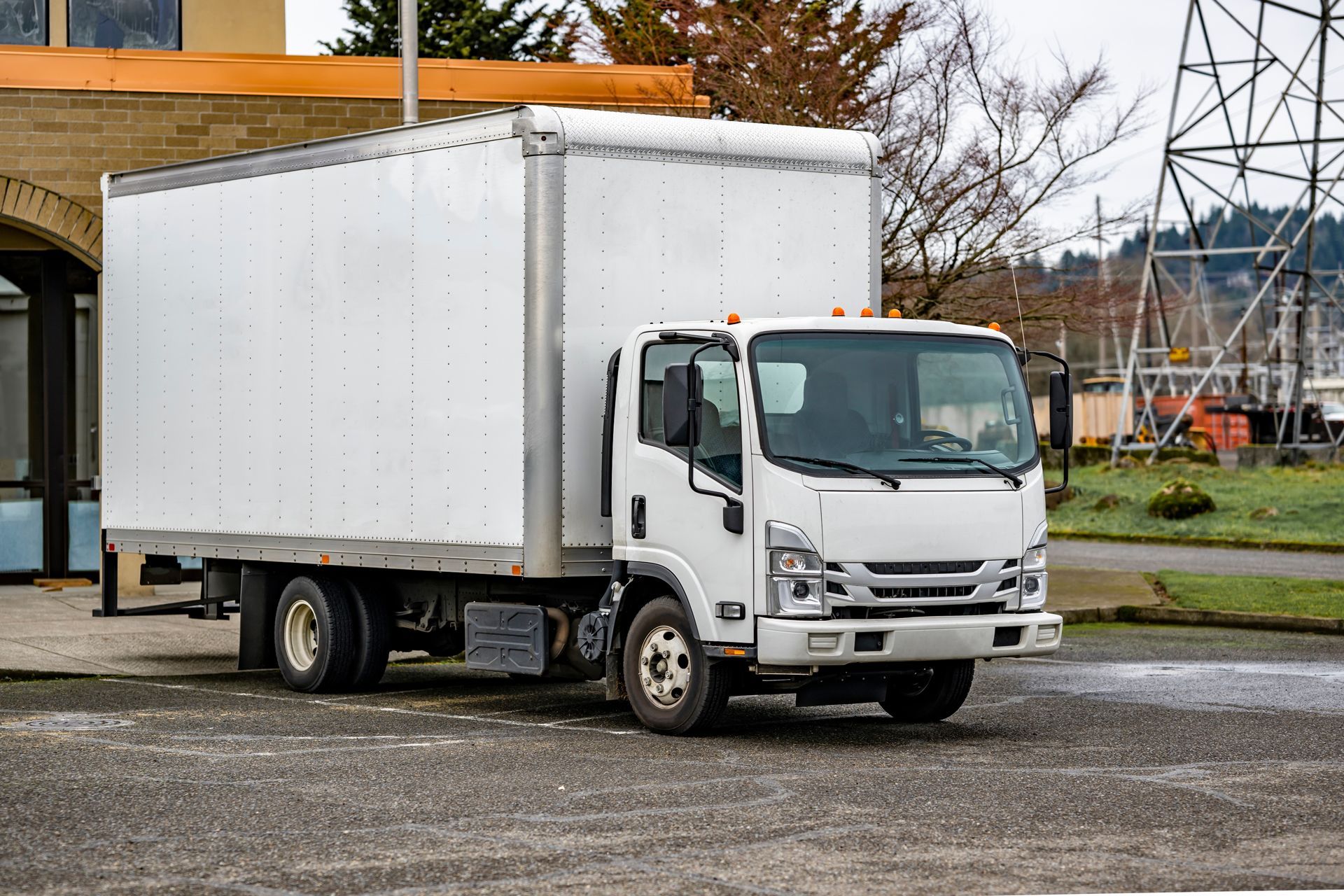 White box truck parked on a gravel lot near a building.