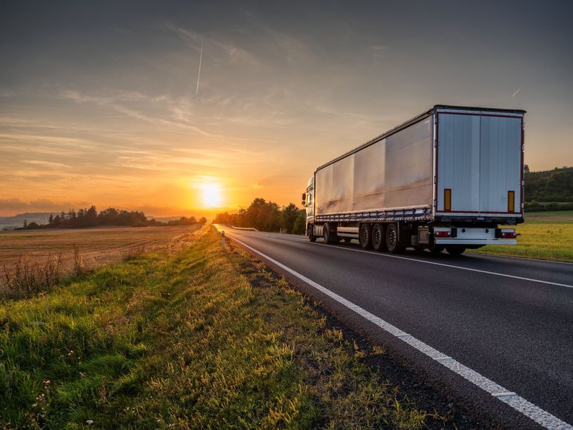 Semi-truck on a highway at sunset, passing through fields.