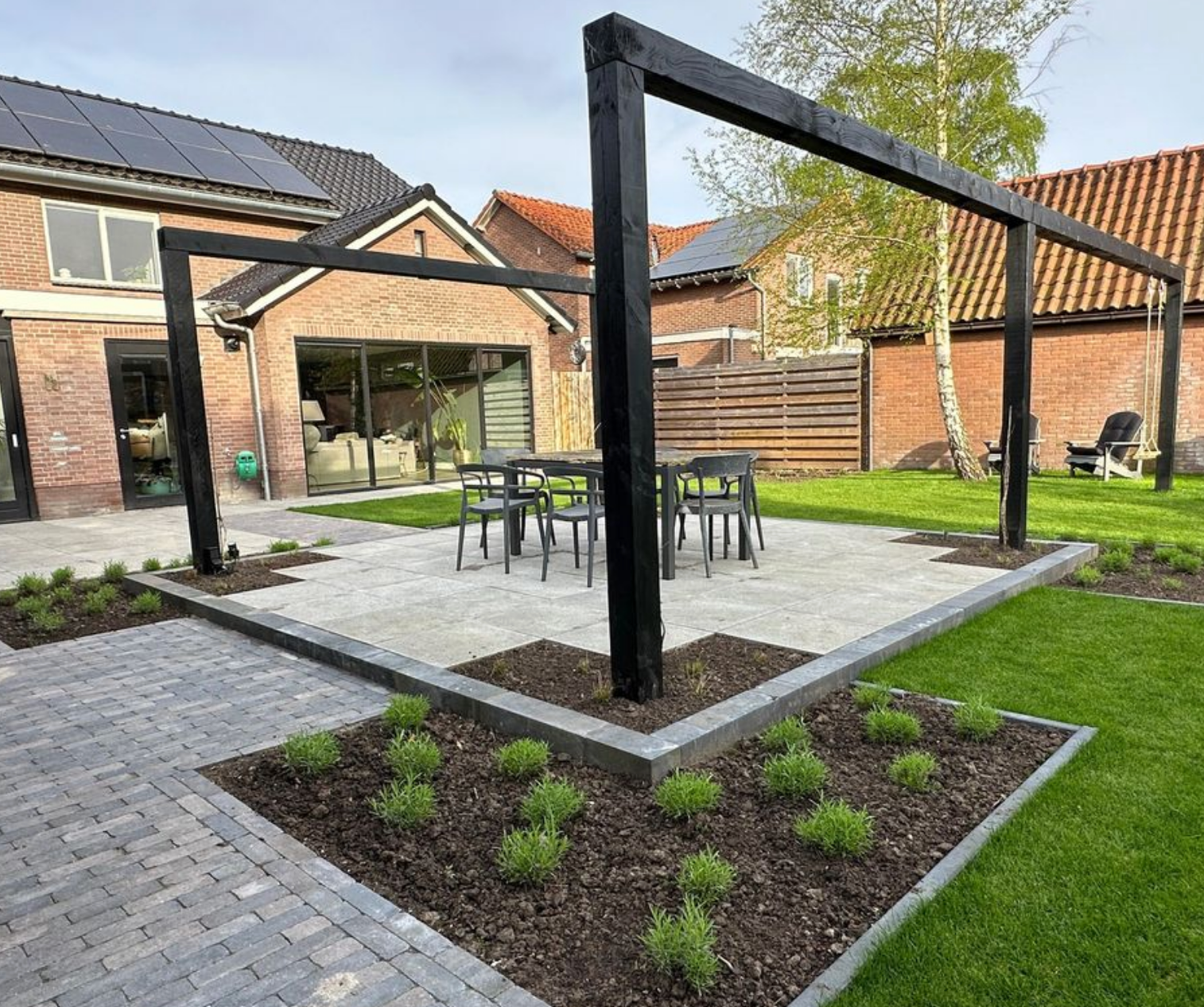 Er is een terras met een pergola en groot gazon in de achtertuin van een huis.