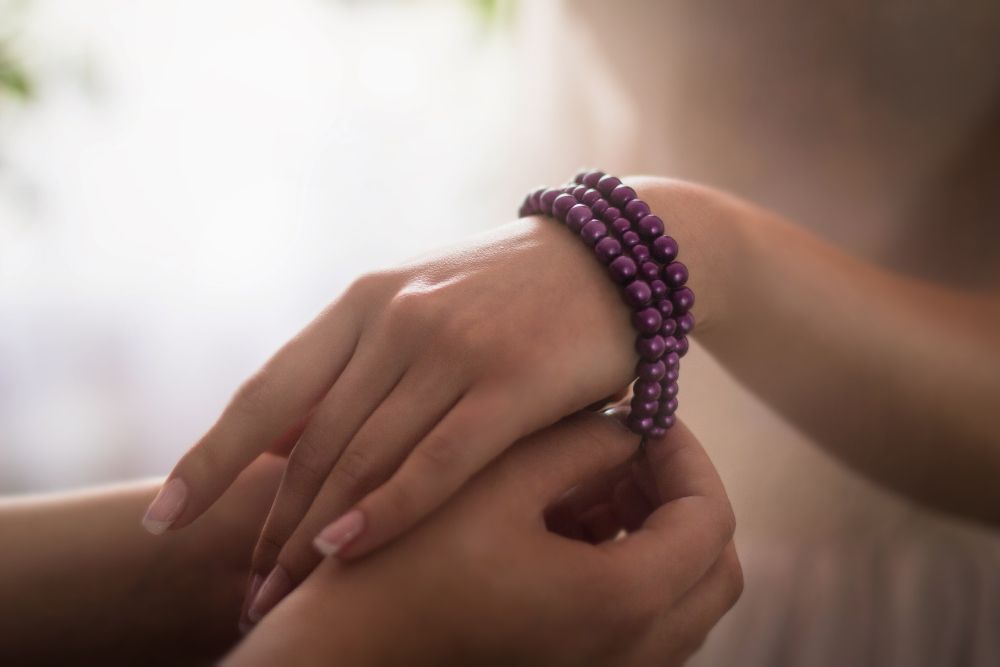 Two hands gently holding, with a purple beaded bracelet on the wrist.
