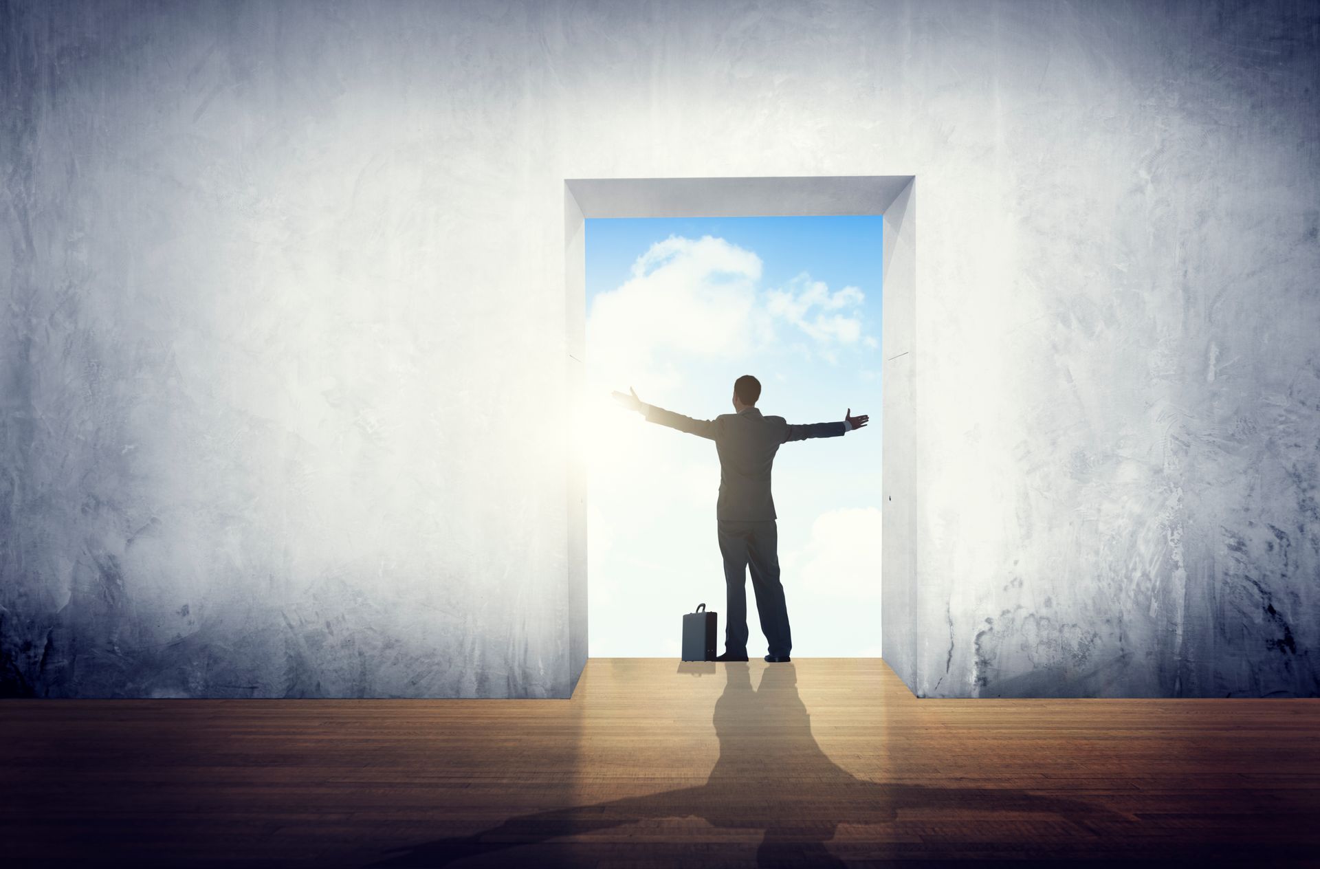 Silhouetted person with arms outstretched in a doorway, bright sky beyond, inside a bare room with a wooden floor