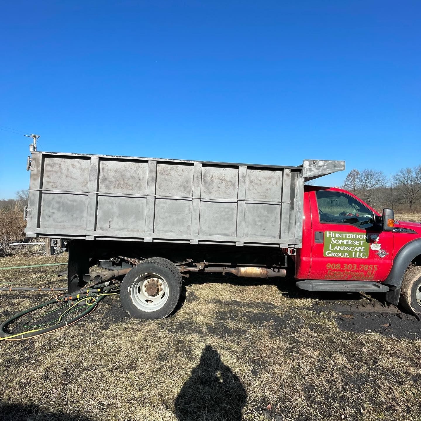 A red dump truck is parked in a field with a blue sky in the background.