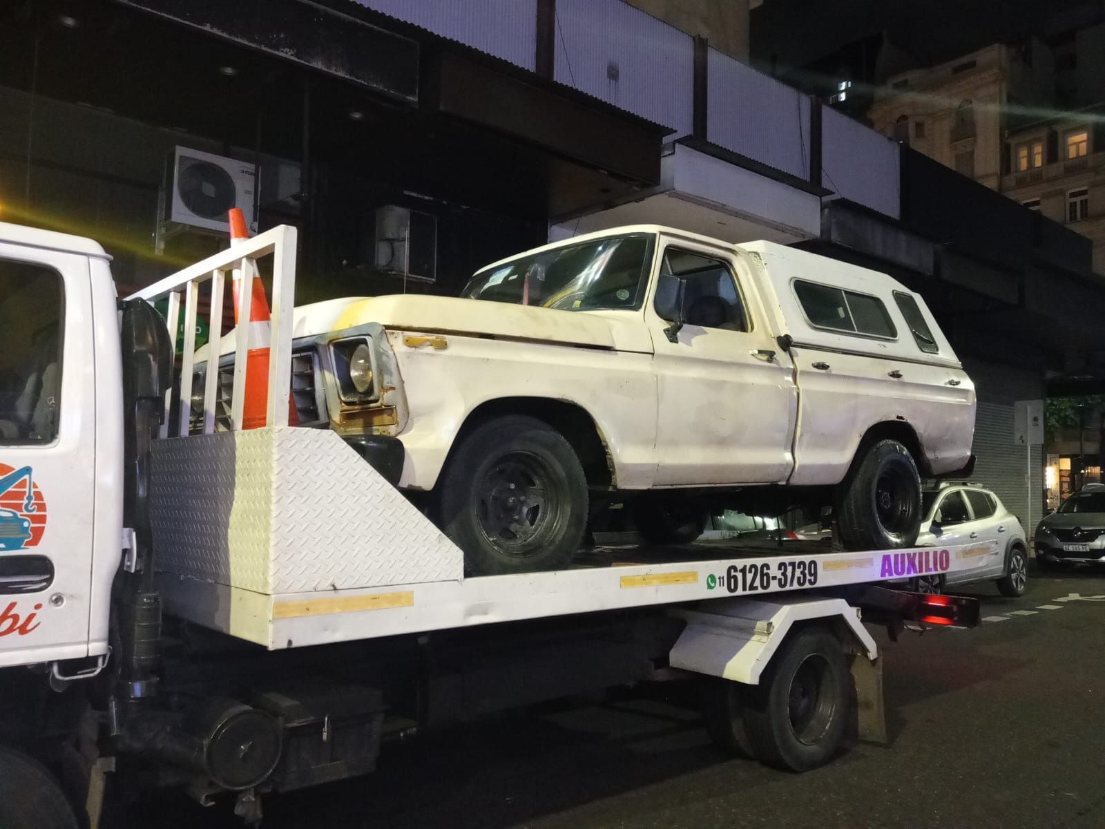 SUV blanco sobre una gr&uacute;a por la noche en una calle urbana, con otra furgoneta parcialmente visible cerca