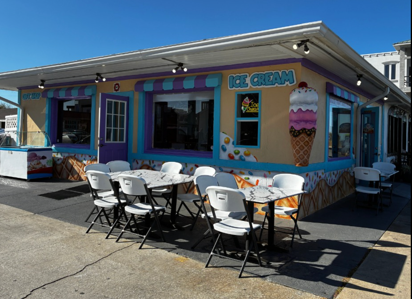 Colorful ice cream shop with outdoor tables and chairs on a sunny street corner