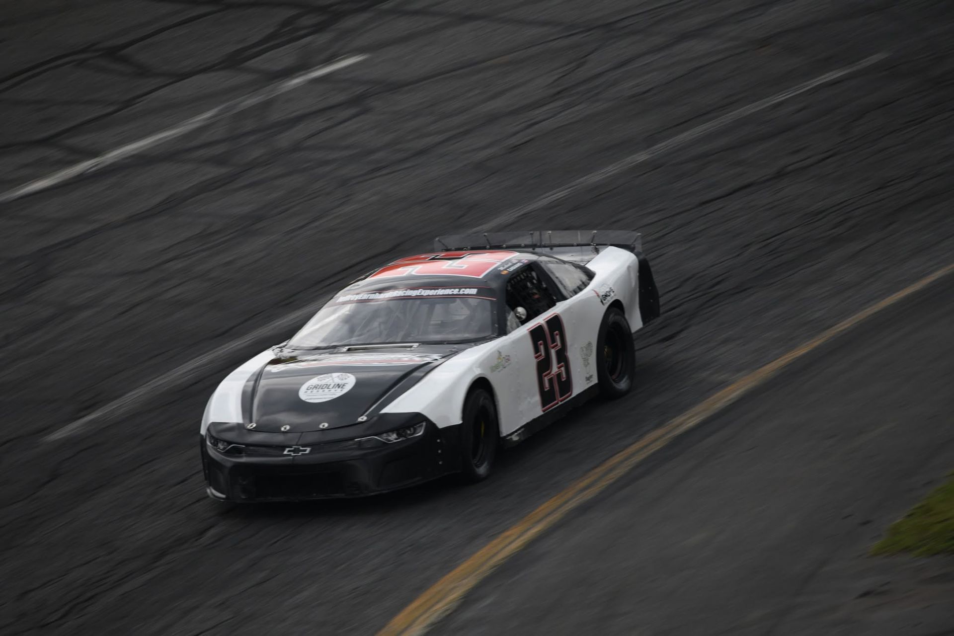 White and black race car with red roof speeding on a wet track during a turn