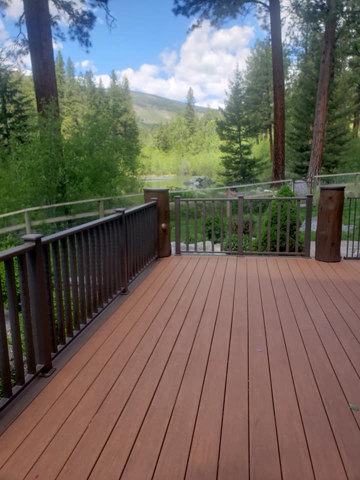 Brown deck with railings overlooking a green valley and mountains under a blue sky.