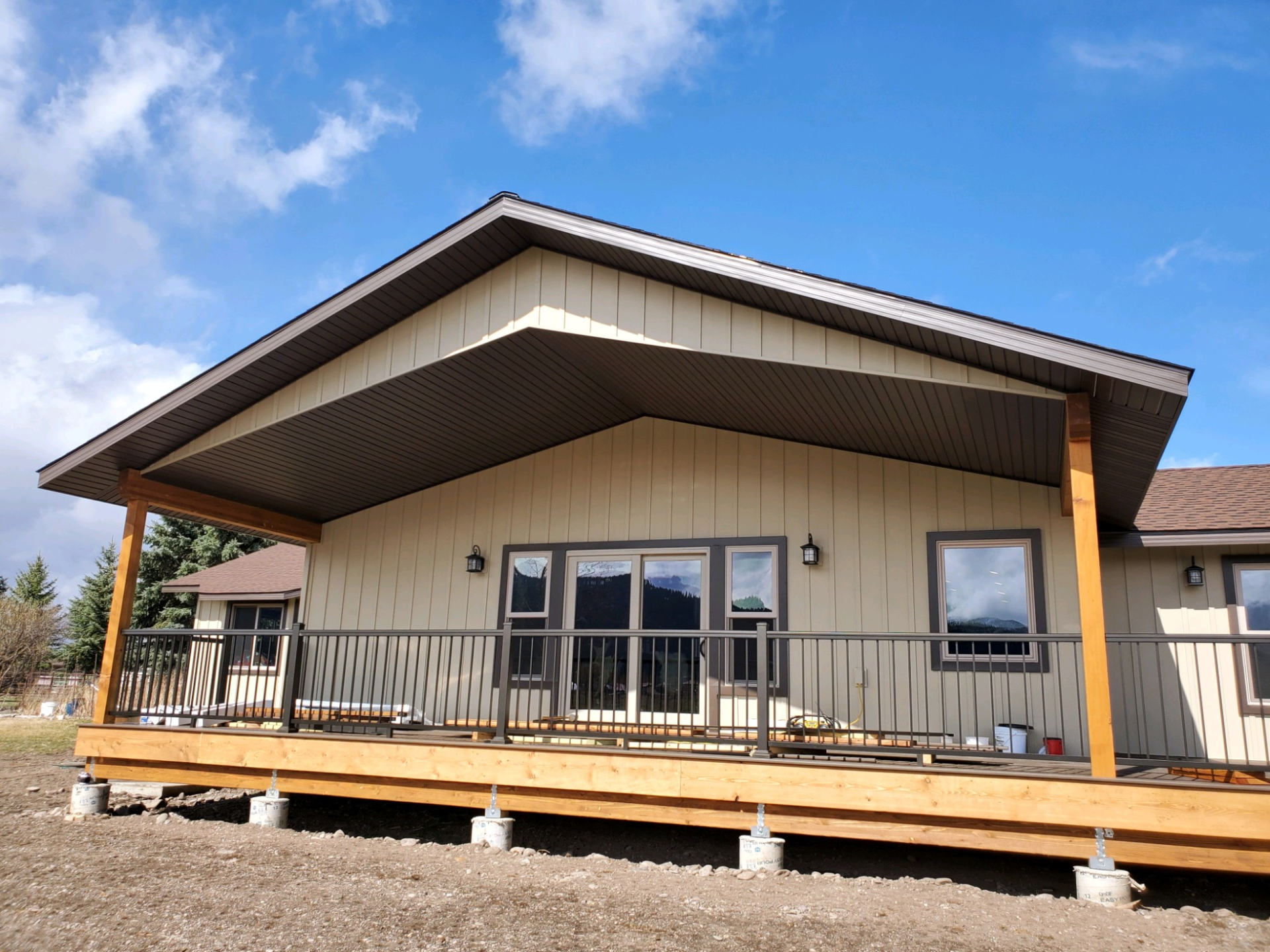 Tan house with a covered porch and railing, supported by wooden beams.