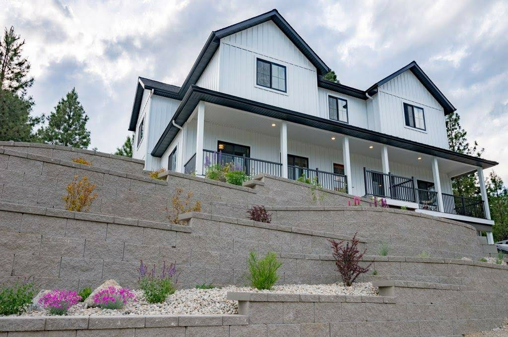 White farmhouse with black trim, built on a terraced retaining wall, set against a cloudy sky.
