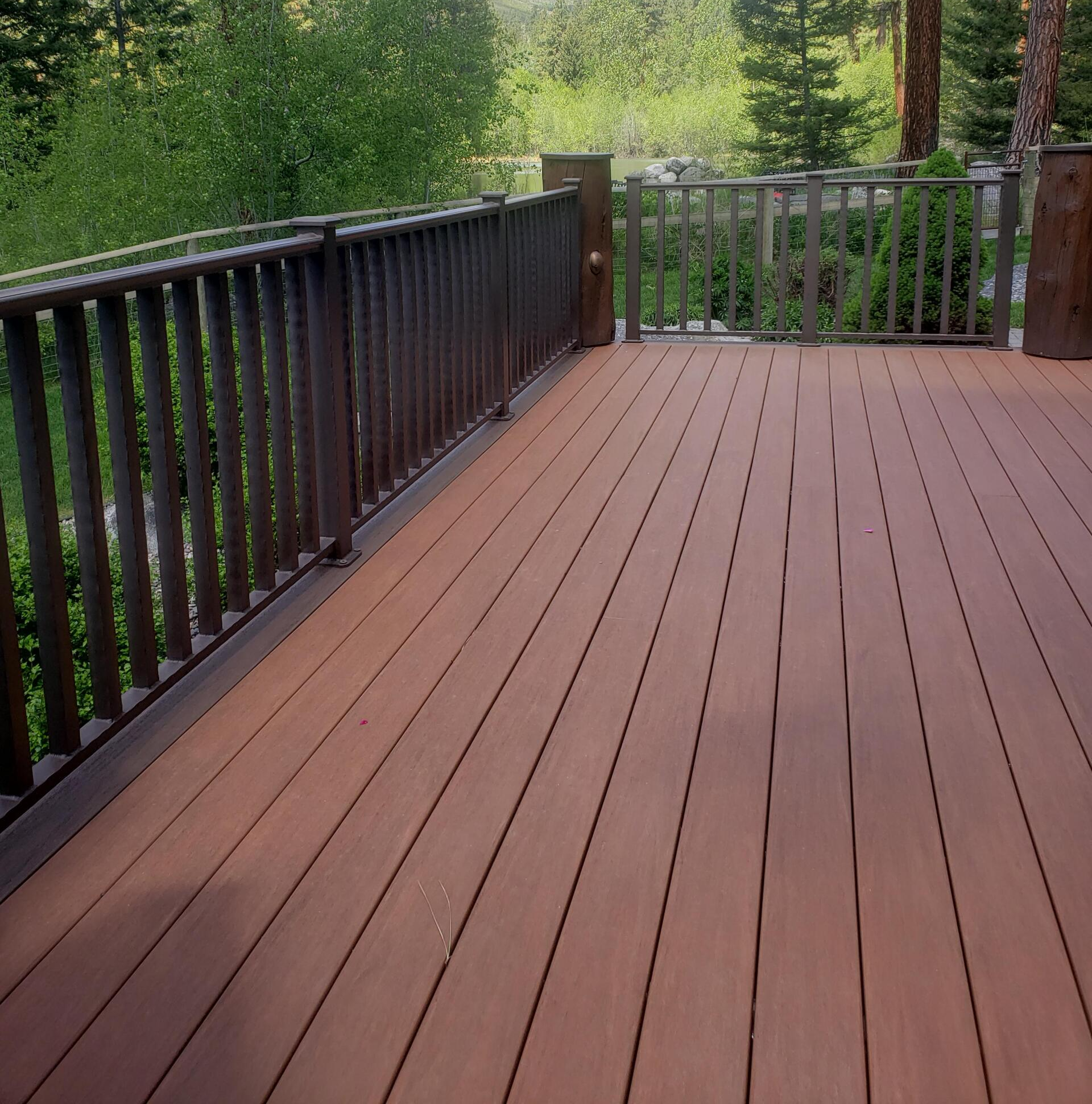 Wooden deck with brown planks and railing, overlooking trees and greenery.