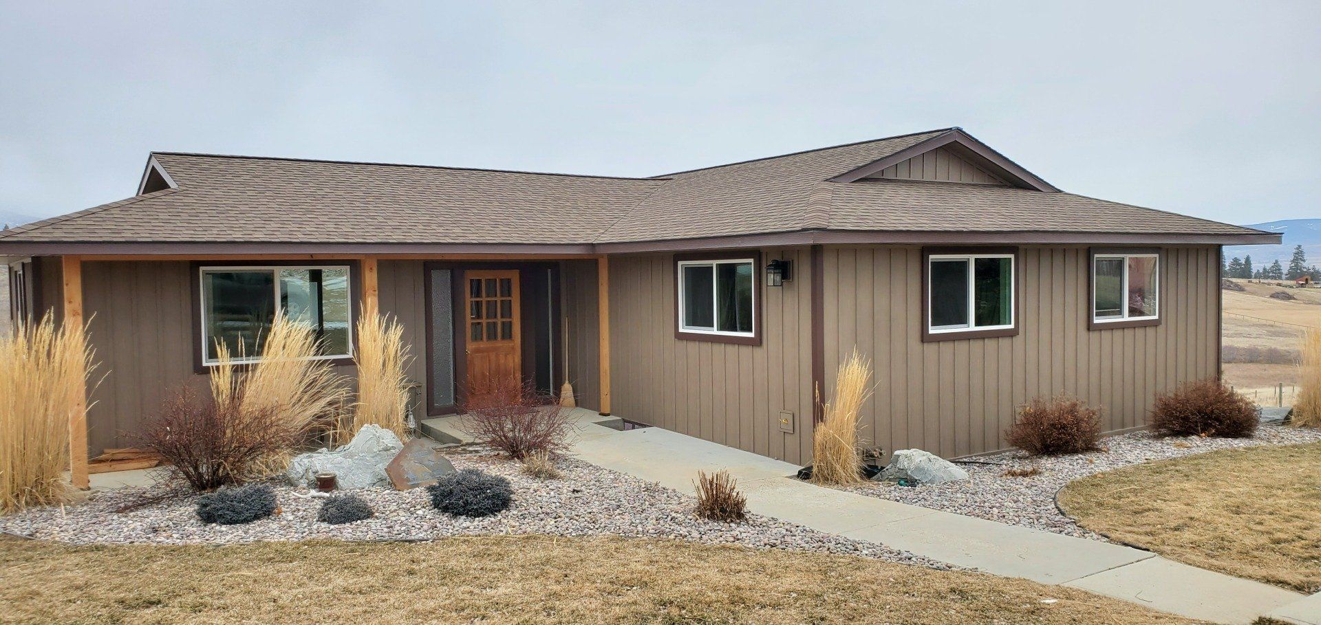 Brown house with brown roof, windows, and a concrete pathway, set in a dry landscape.