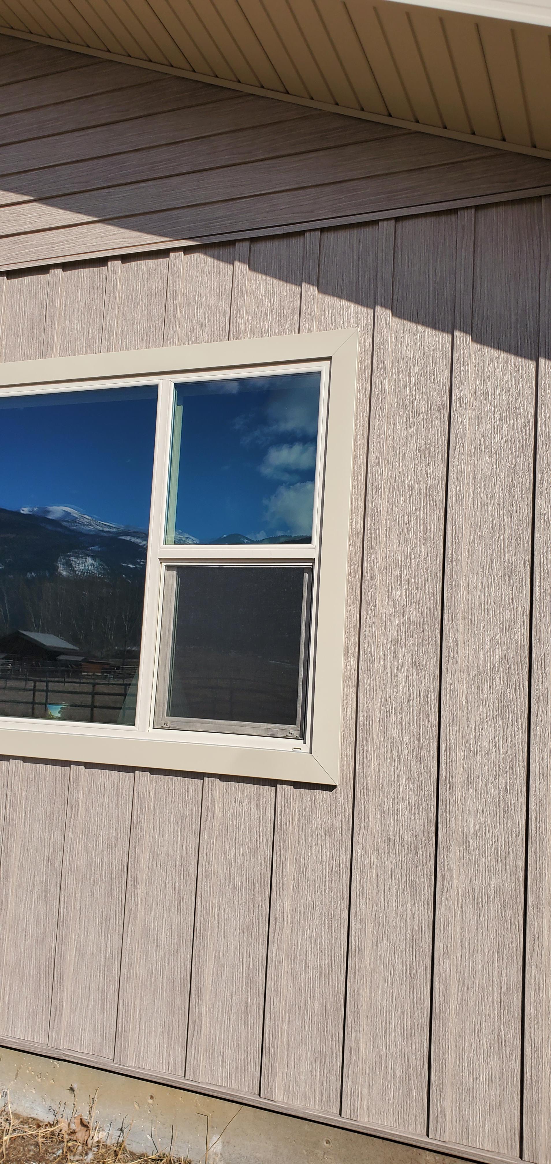 A building with a window reflecting a mountain range and blue sky.