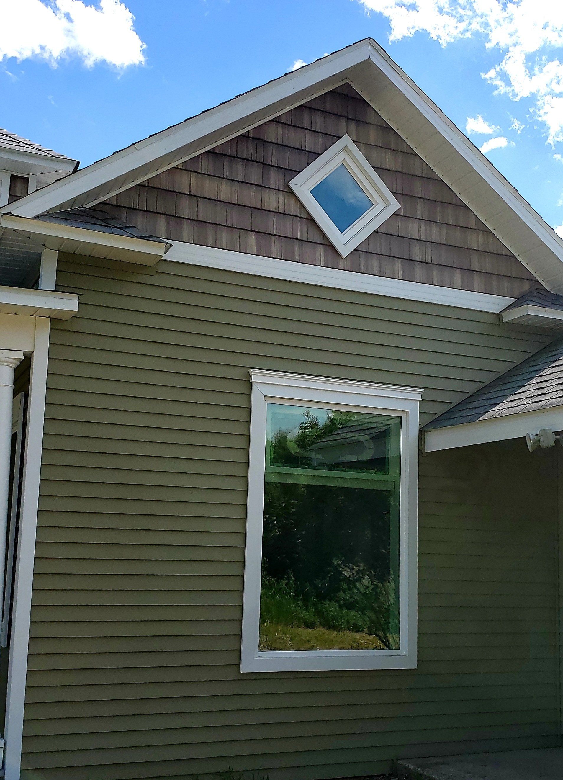 Green clapboard siding on house with a large window and a diamond-shaped window in the gable.