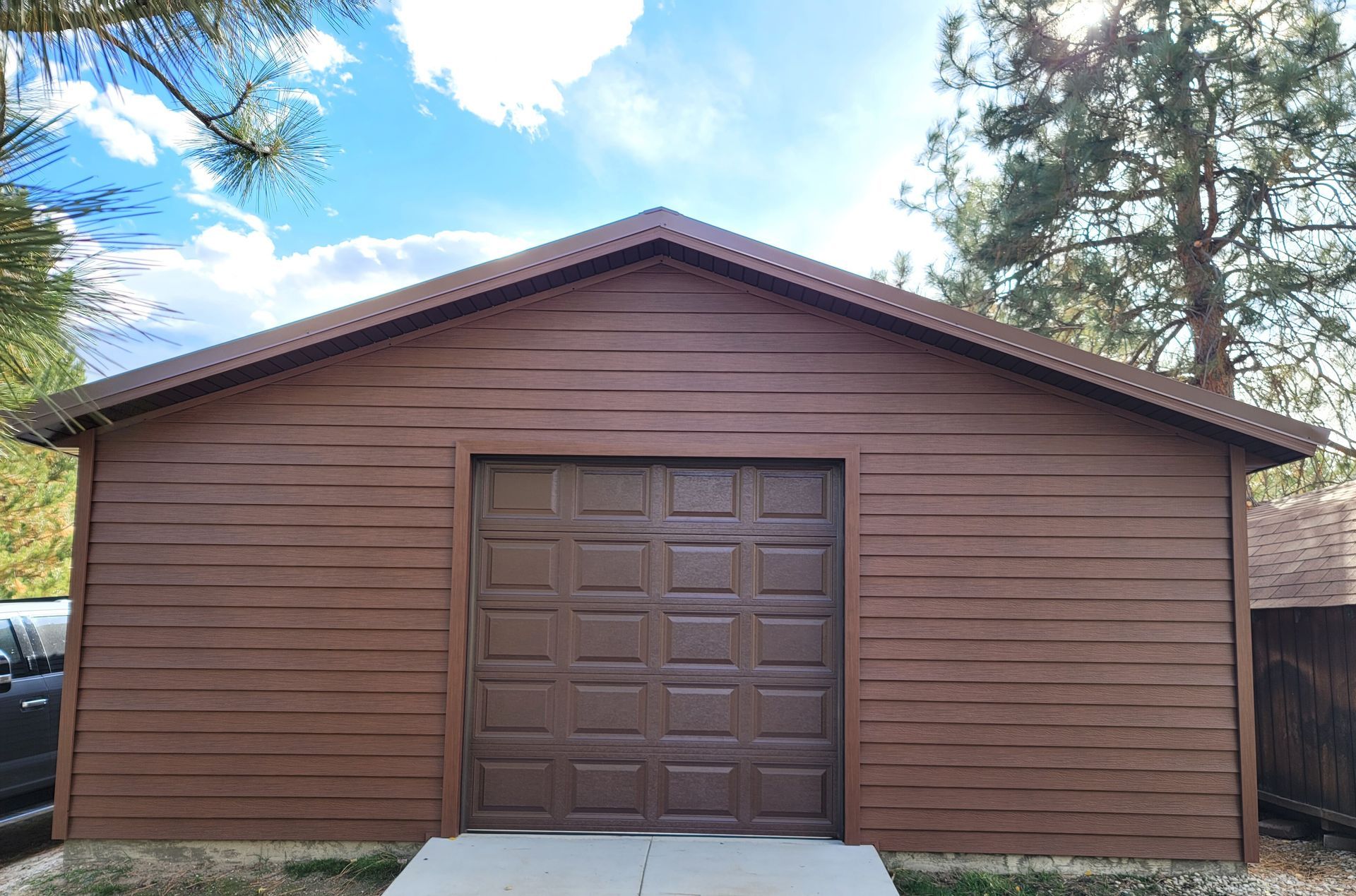 Brown garage with matching door, siding, and roof under a blue sky.