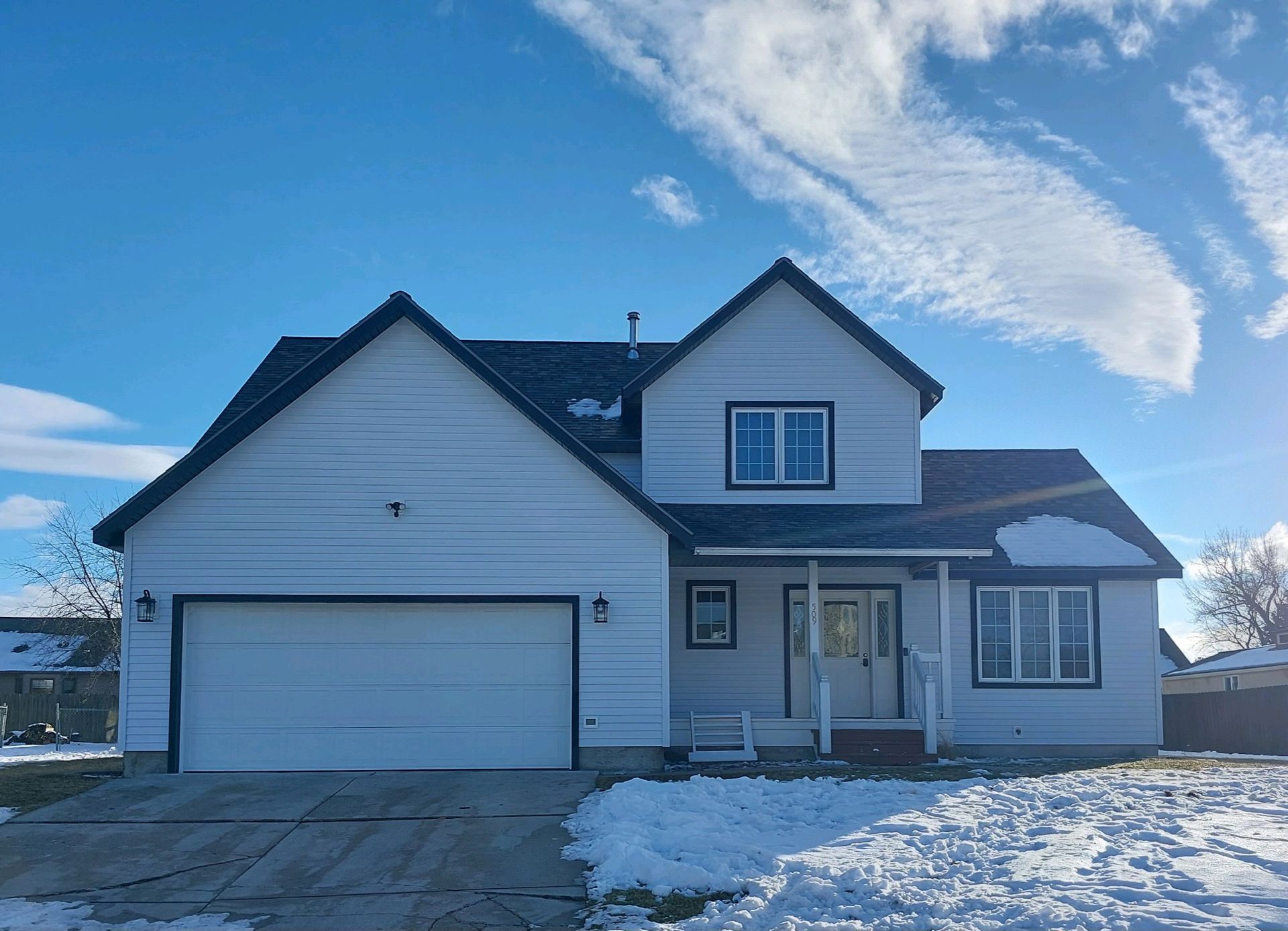 White two-story house with black trim and a garage, set against a bright blue sky with patchy snow on the ground.