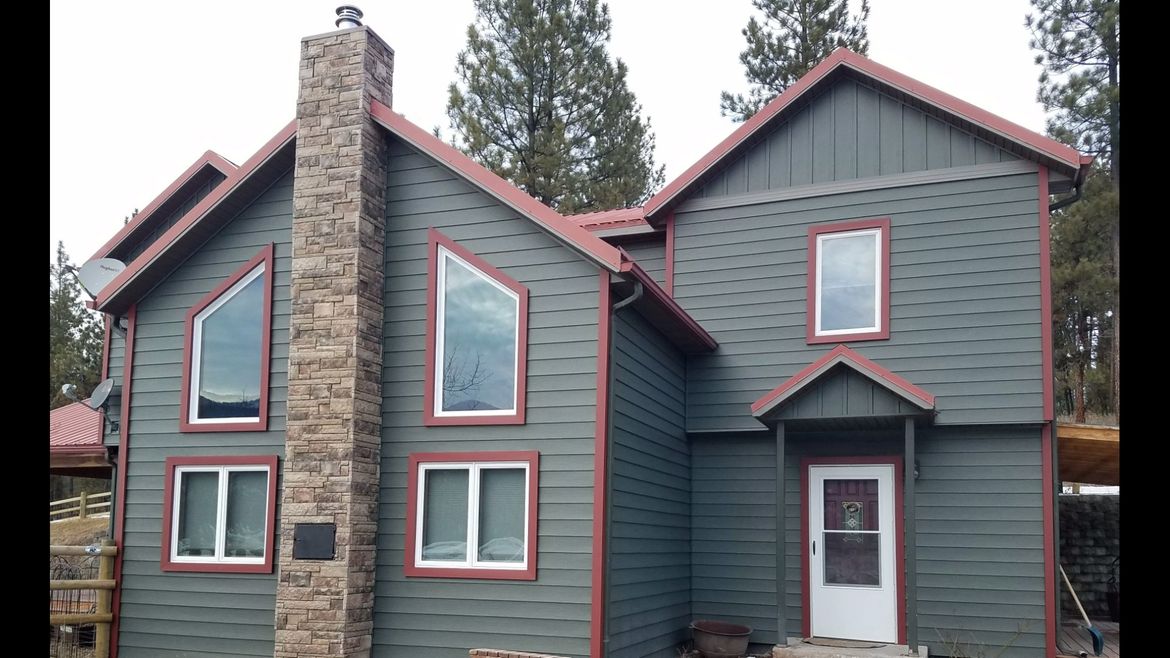 Green house with red trim, stone chimney, and multiple windows.