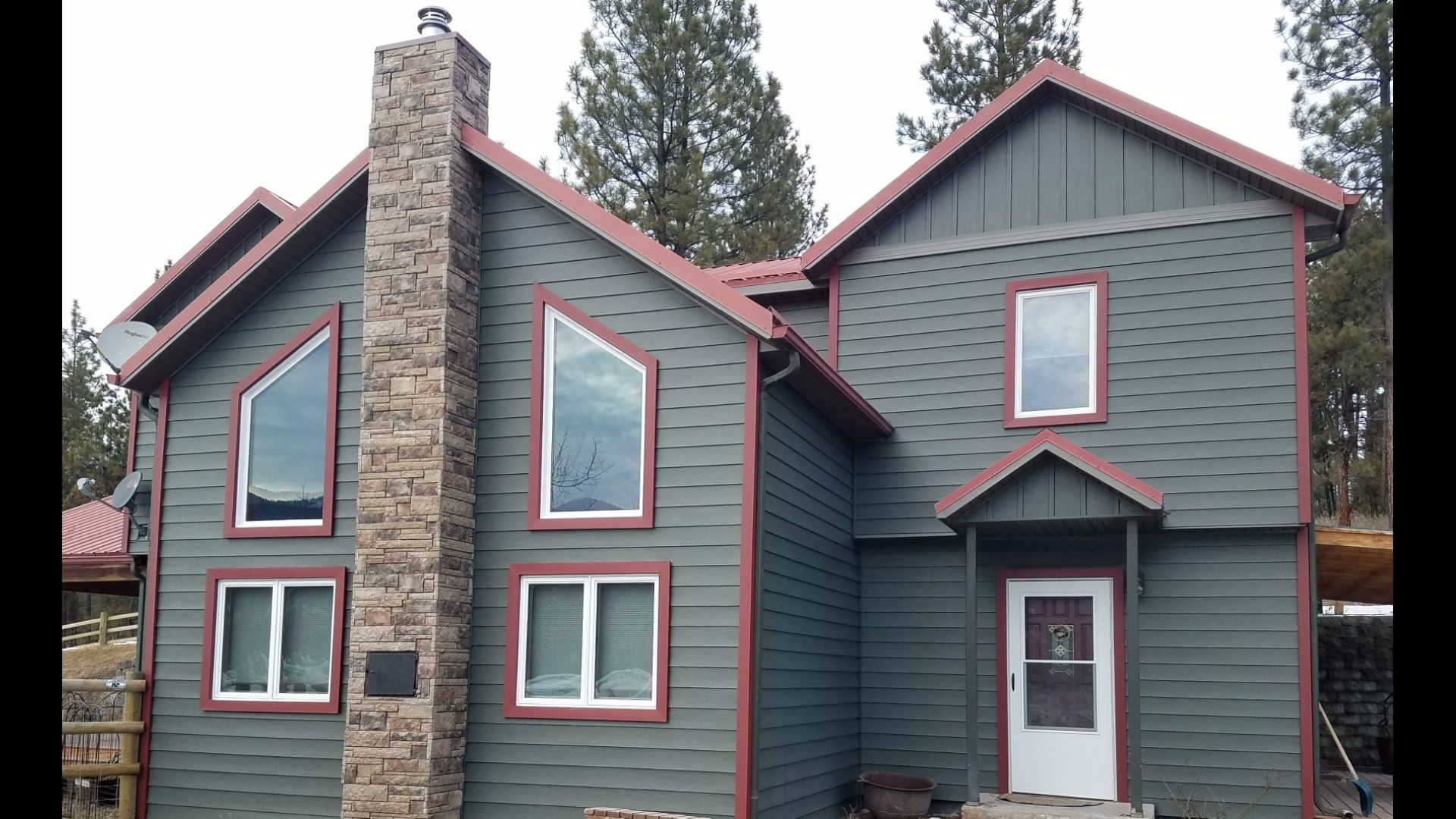 Green house with red trim, stone chimney, and multiple windows.