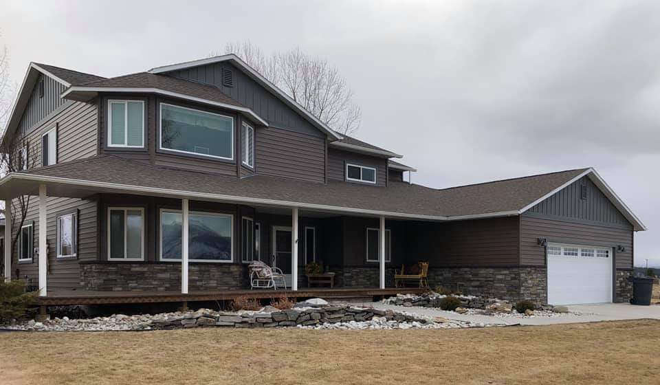 Two-story brown house with a wrap-around porch, bay windows, and a detached garage, under a cloudy sky.