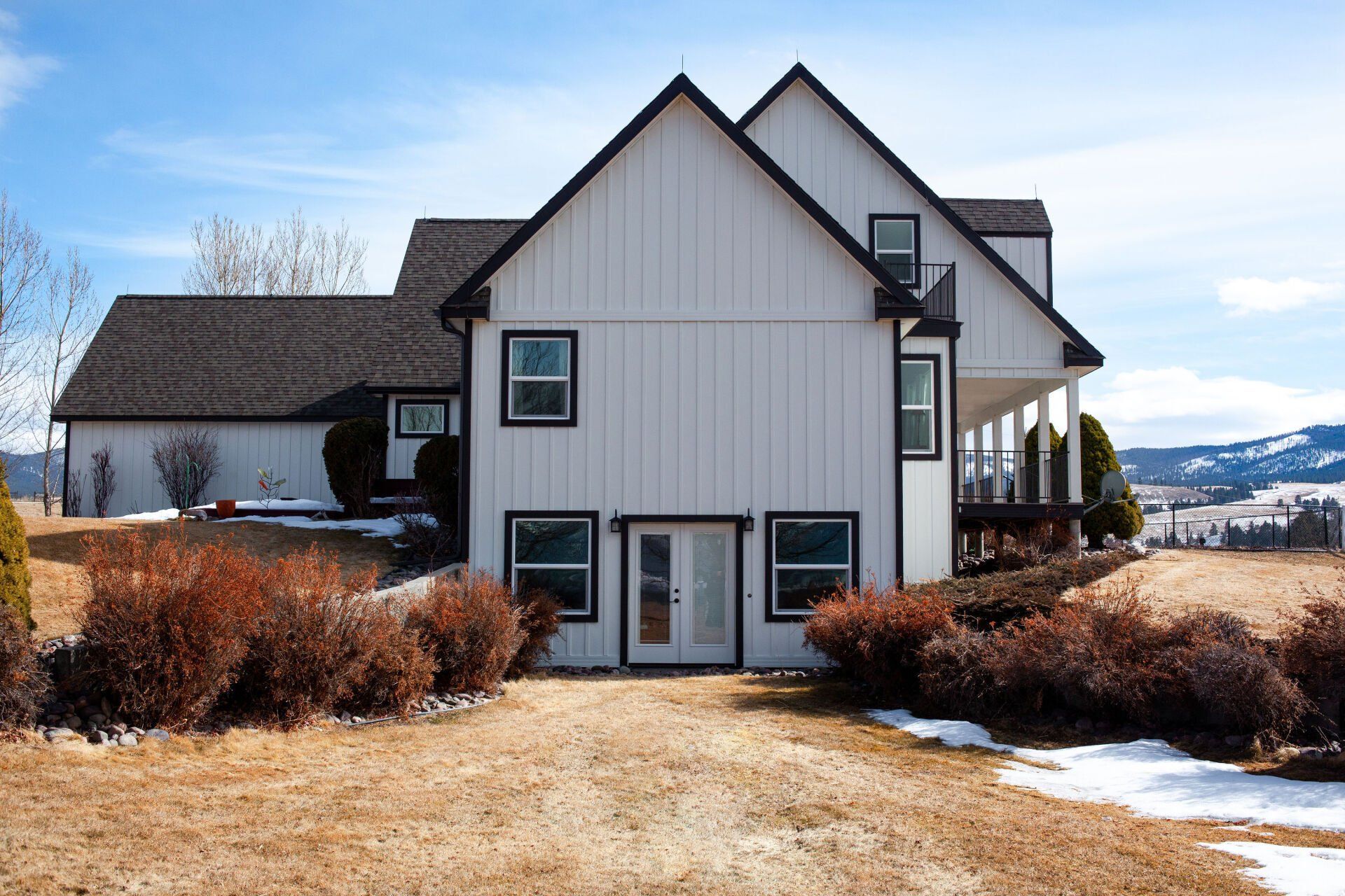 White farmhouse with black trim and a gravel driveway on a sunny day.