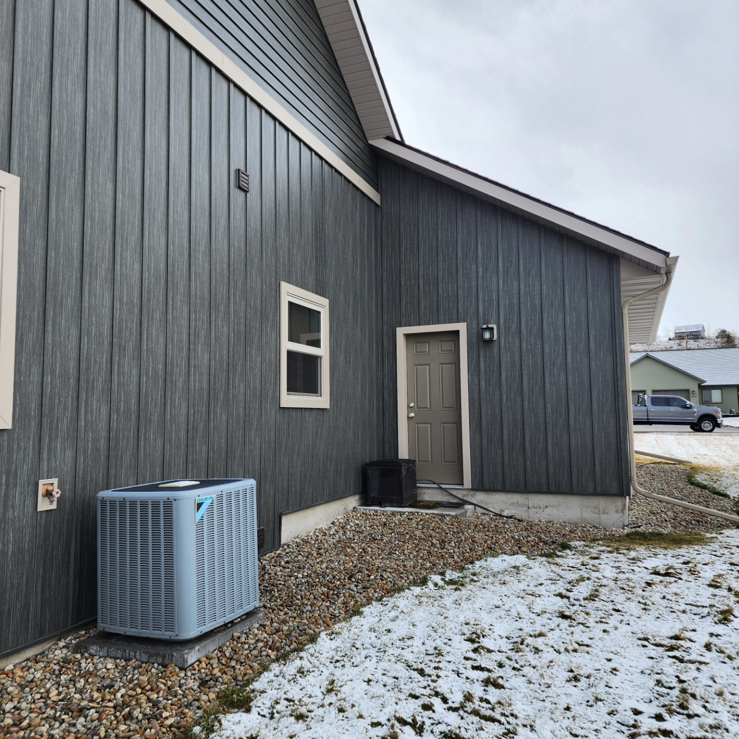 Gray house exterior with siding, air conditioner, and snow on the ground.