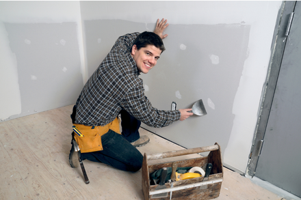 Contractor repairing and patching drywall inside a residential room